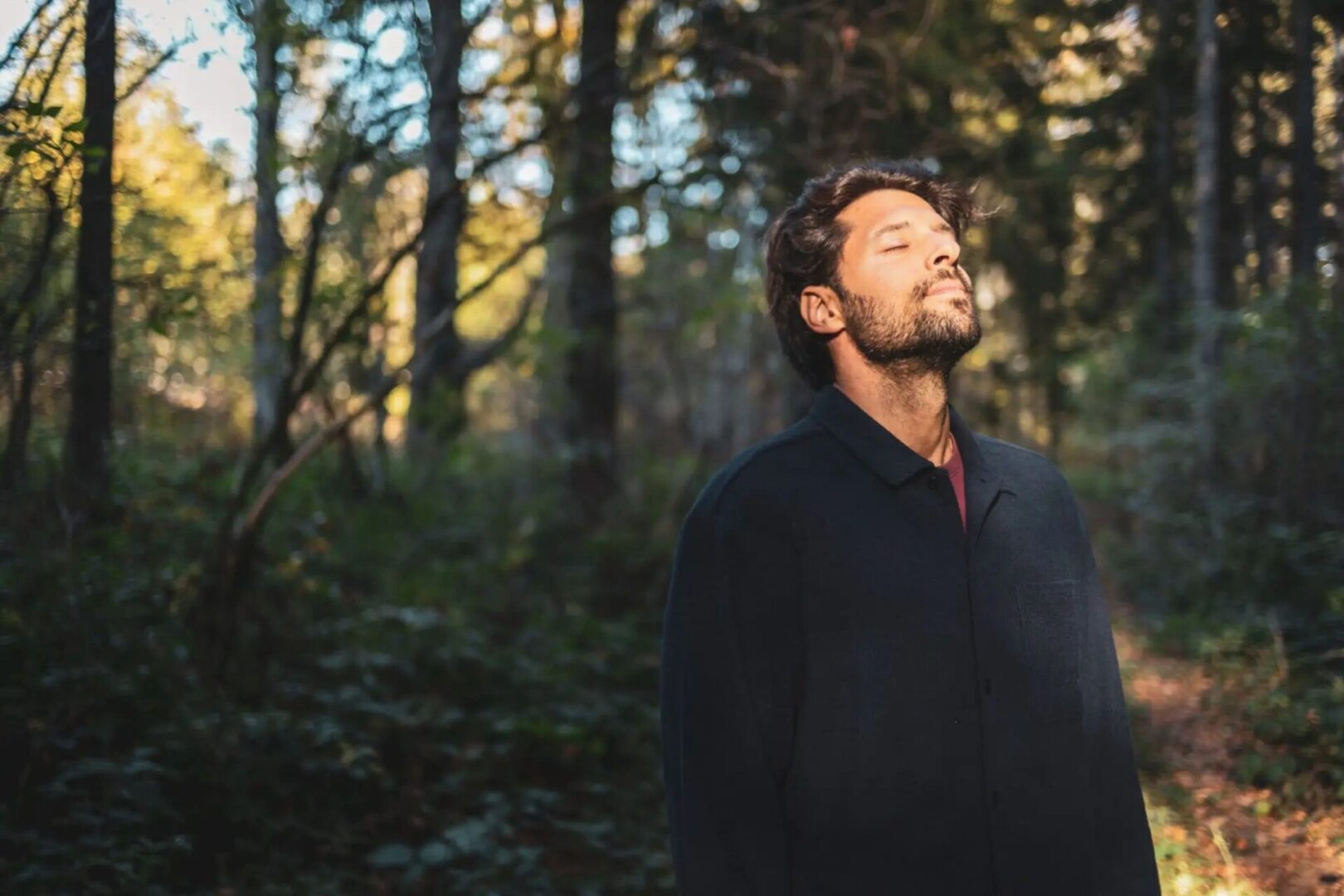 Man enjoying a peaceful moment in the forest with eyes closed.