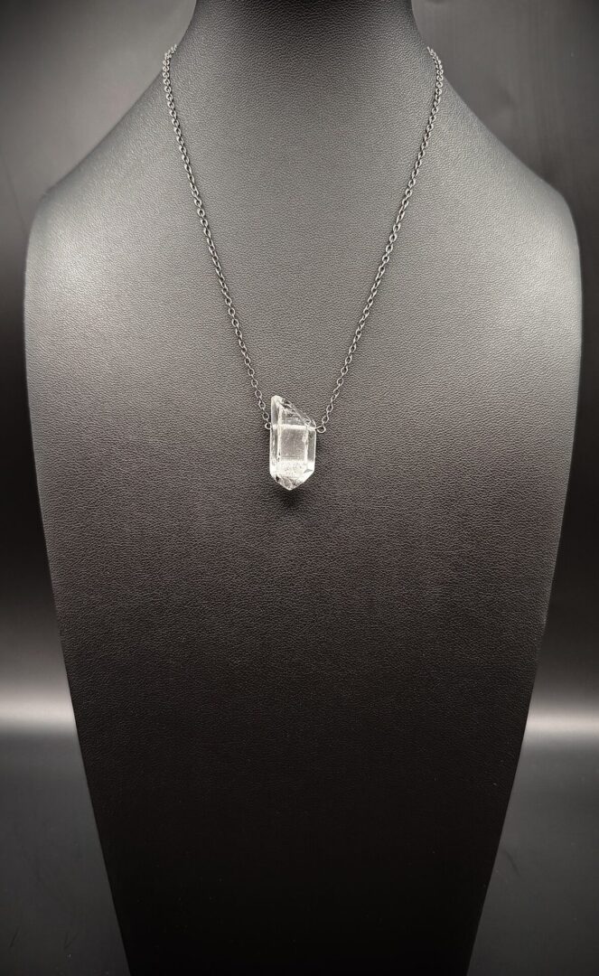 Clear crystal pendant necklace on a silver chain displayed on black stand.