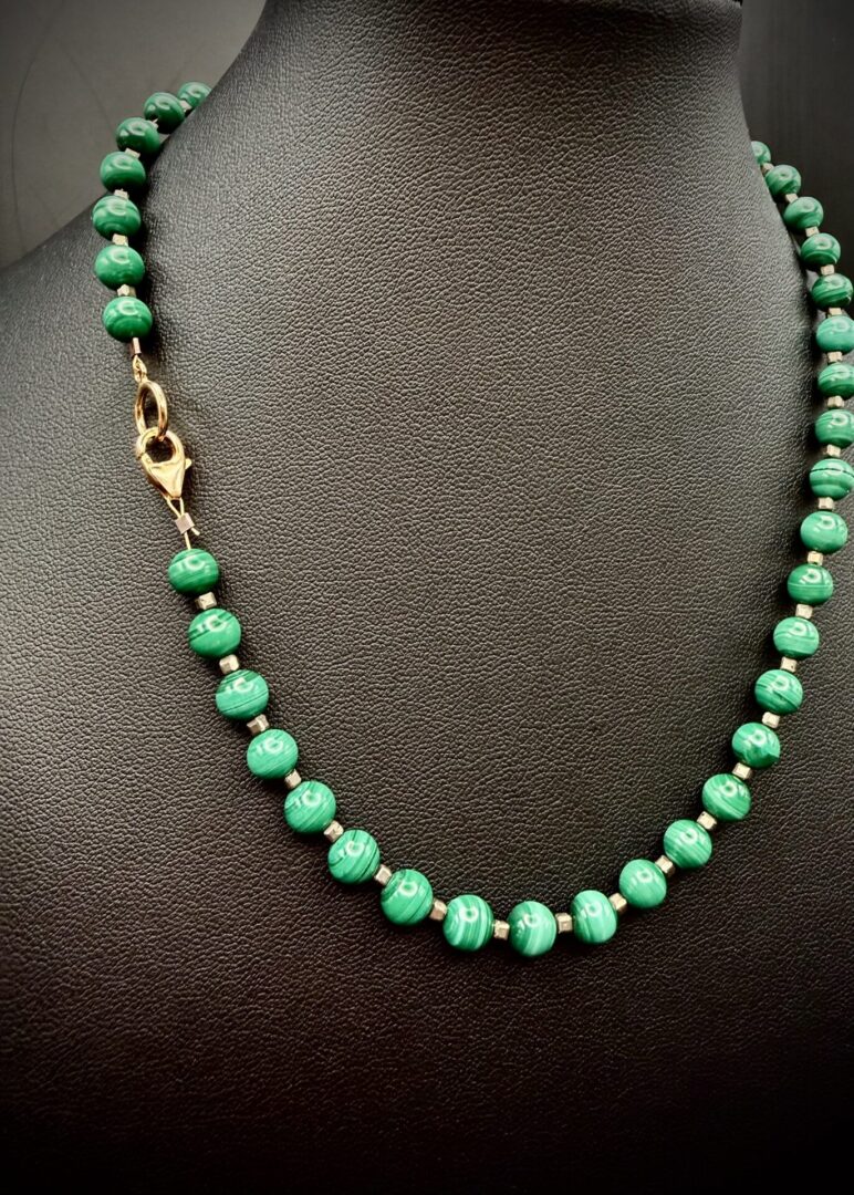 Elegant green bead necklace with gold clasp on black display.