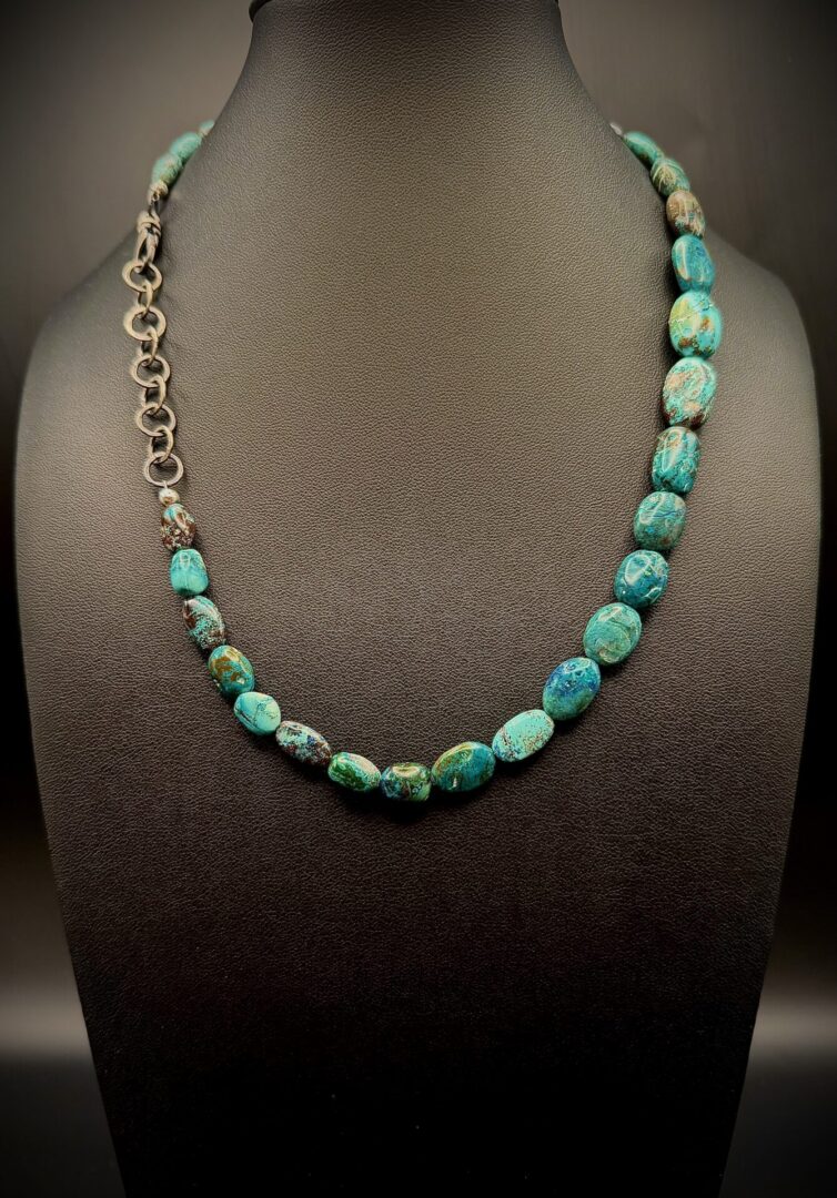 Turquoise bead necklace with a metal clasp displayed on a black stand.