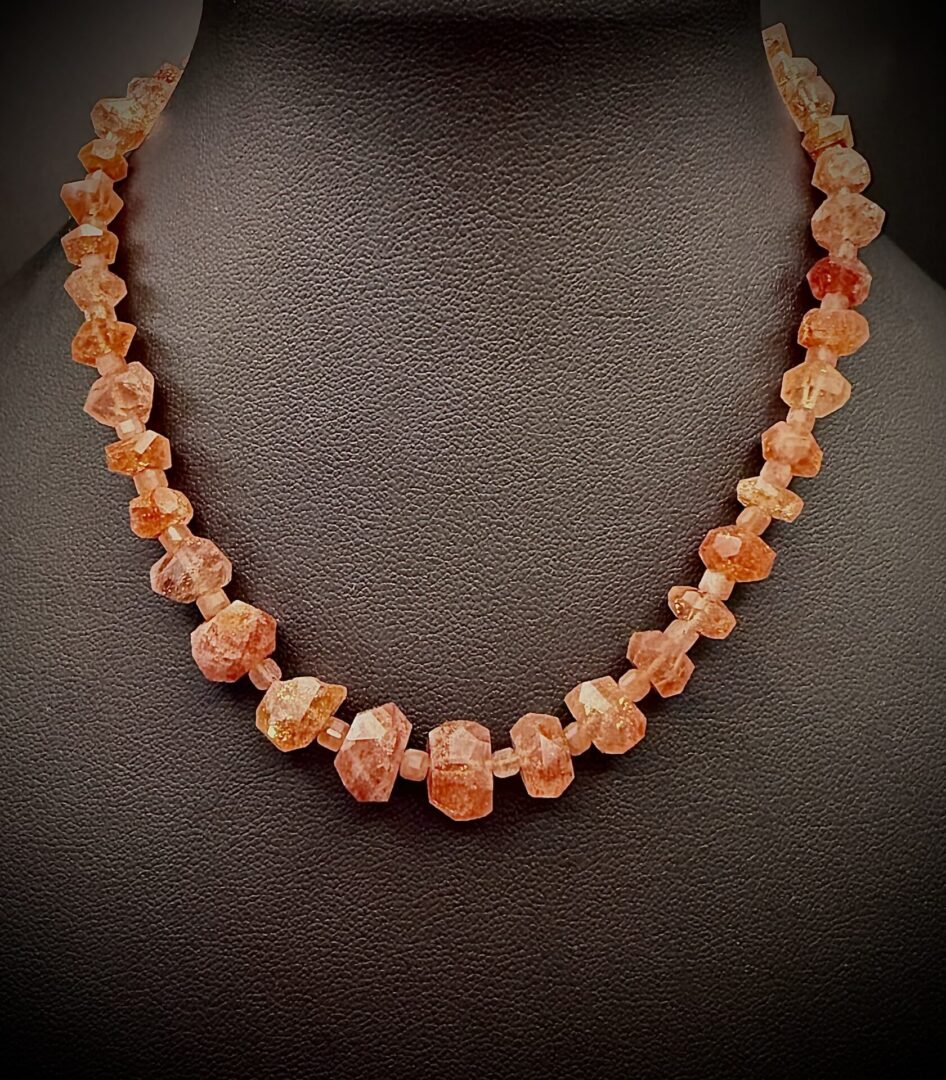 Faceted orange gemstone necklace displayed on a black bust.