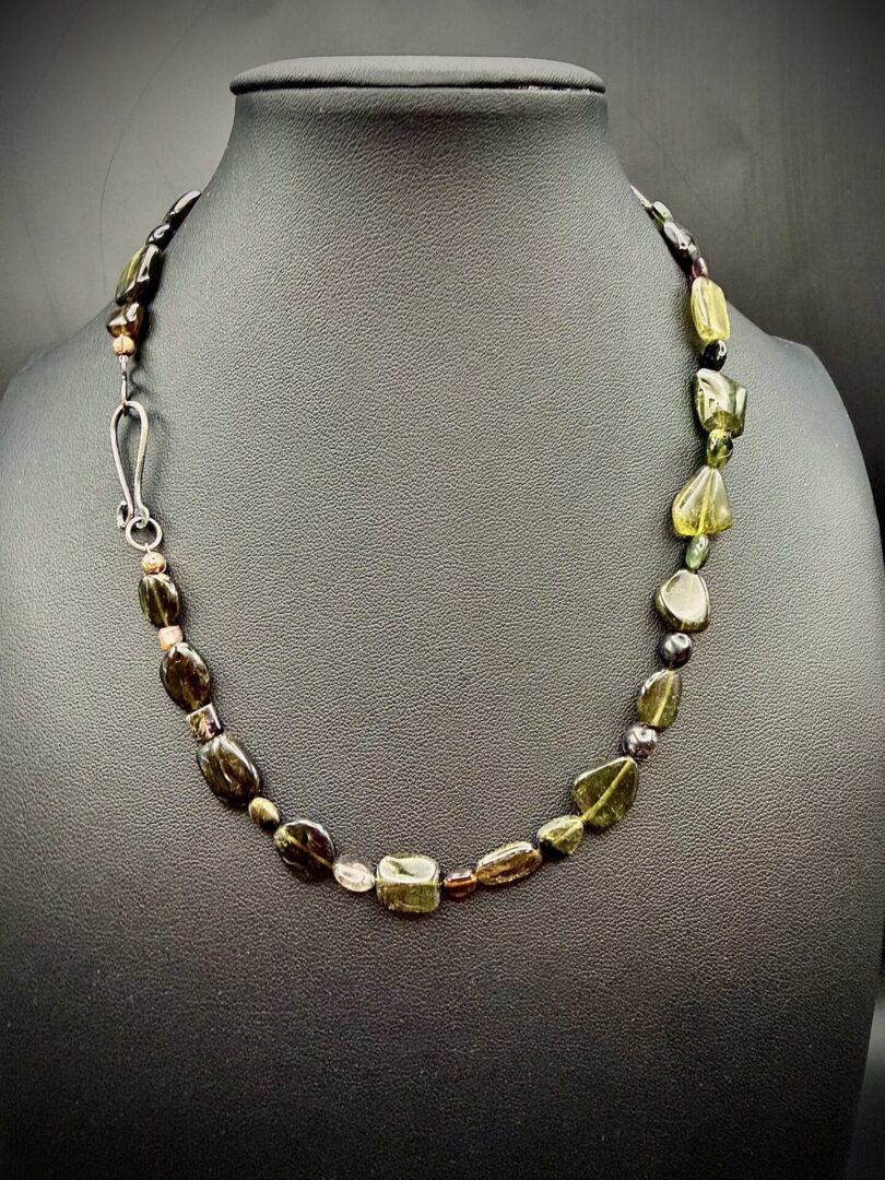 Elegant necklace with green and brown beads on a black display stand.