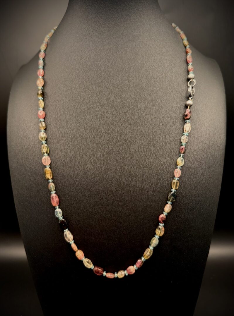 Delicate multicolored beaded necklace displayed on a black bust.