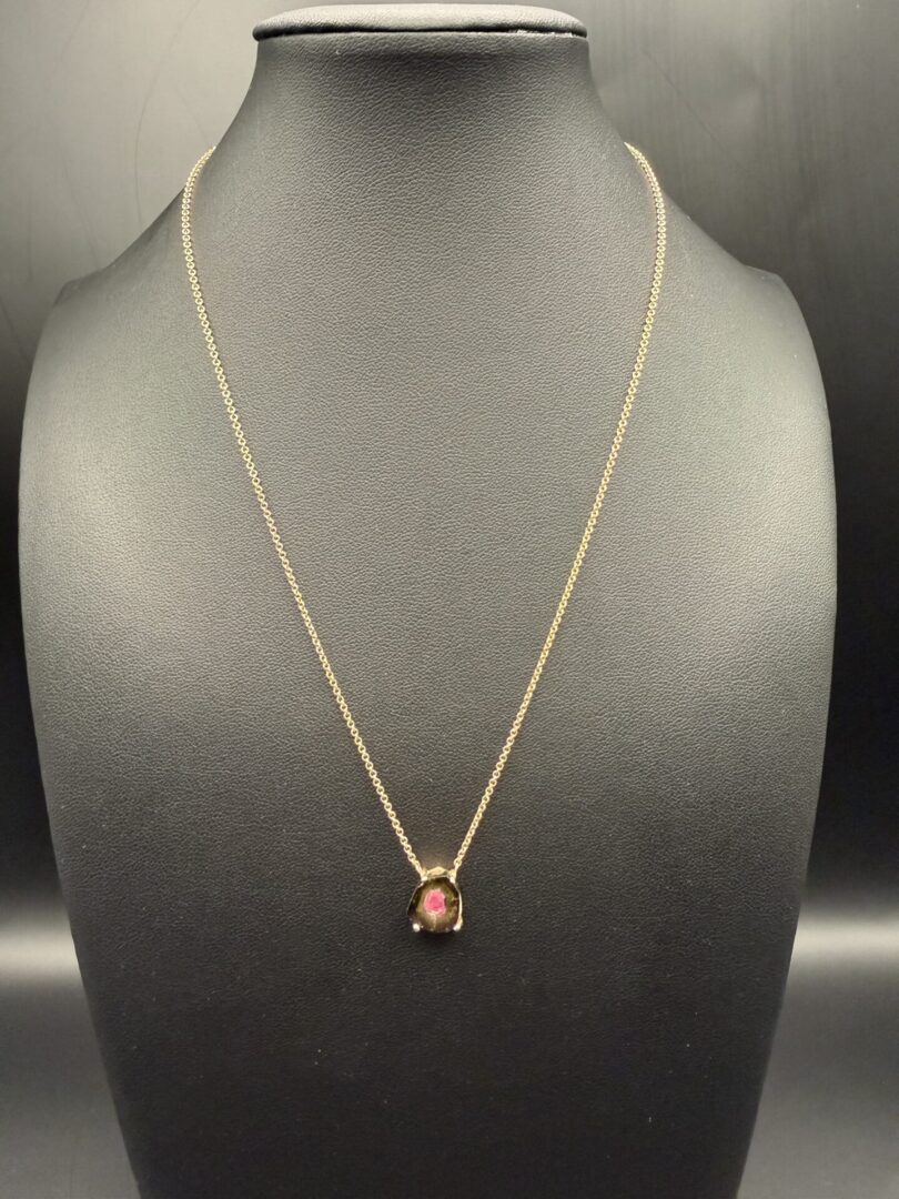 Gold necklace with a unique pendant featuring a pink center stone on black display.