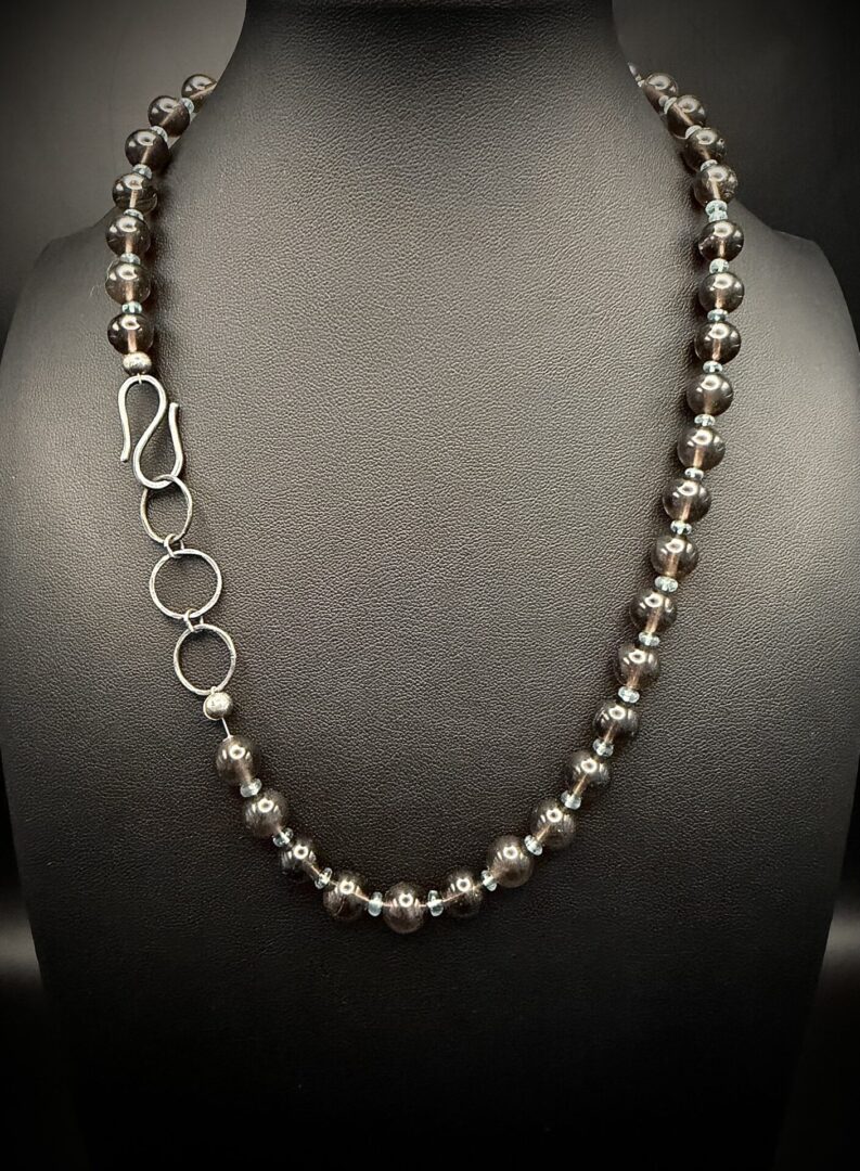 Elegant beaded necklace with dark round beads and silver accents on a black display.