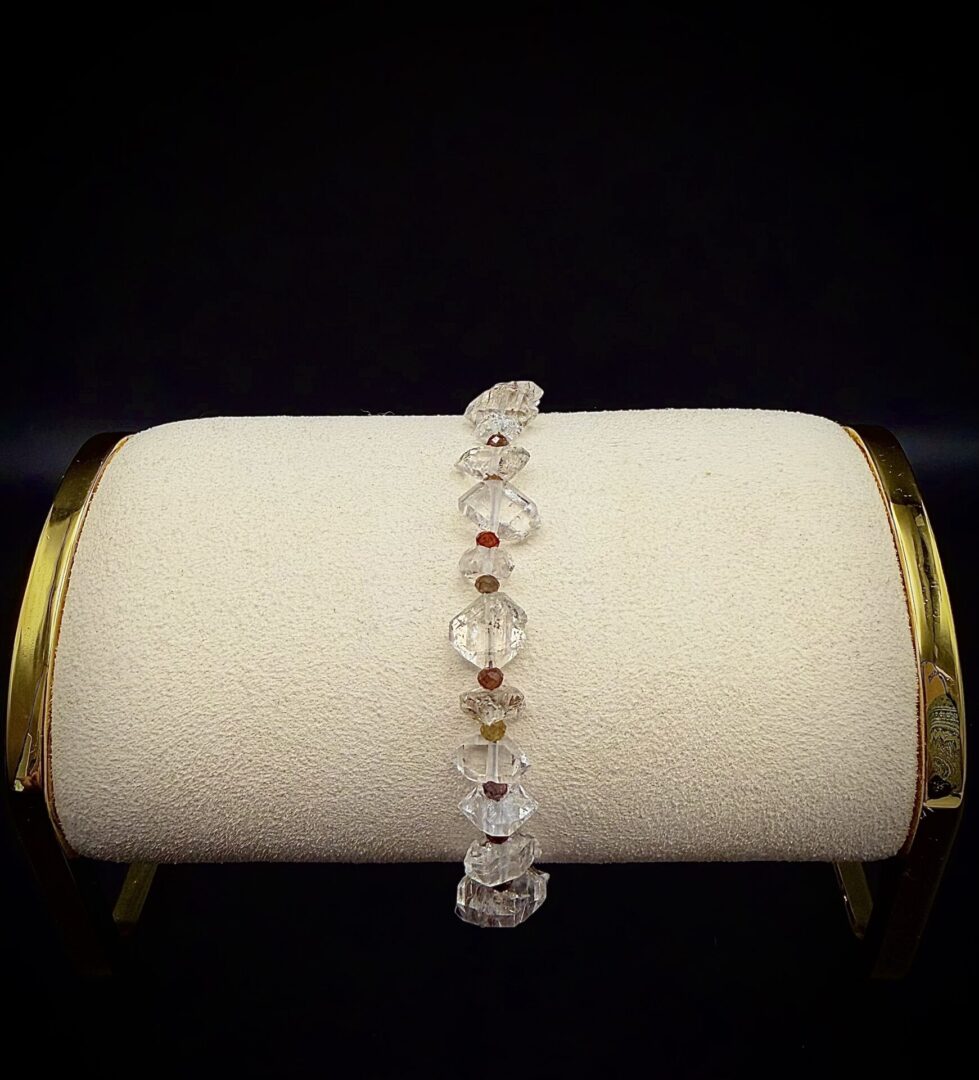 Delicate clear crystal bracelet with small colored beads on a cushioned display stand.