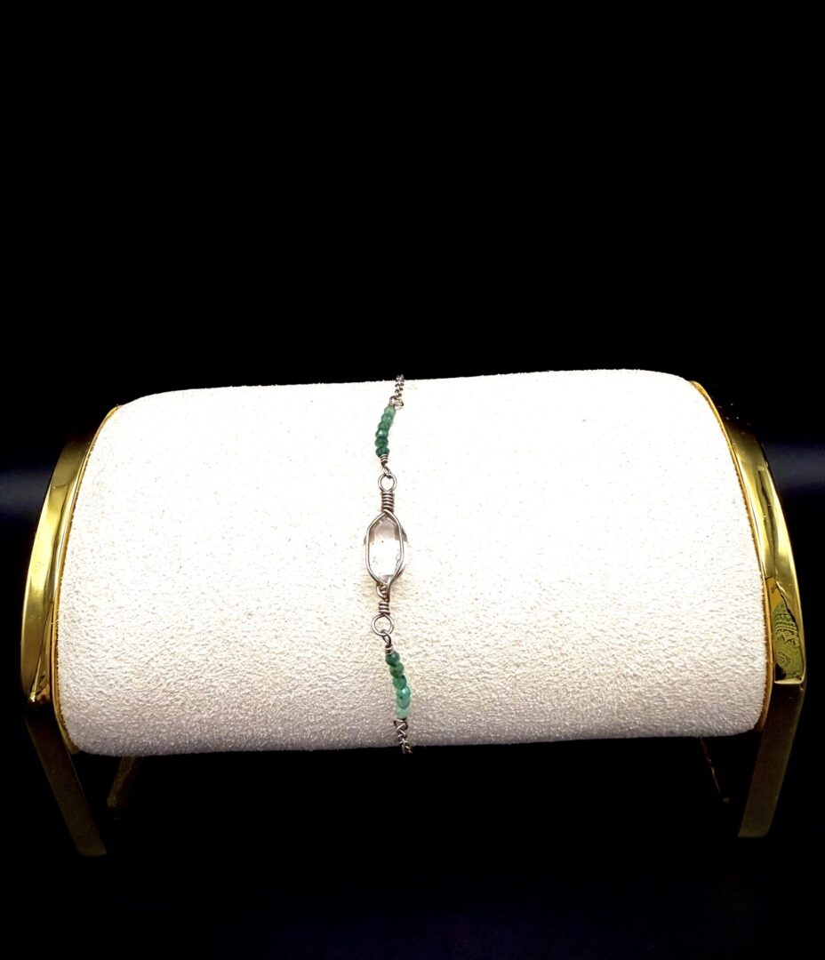 Delicate bracelet with green beads and central clear stone on white display stand.