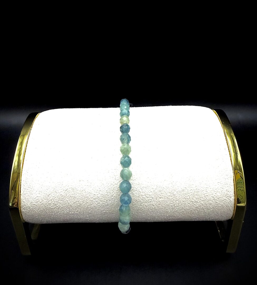 Elegant blue and green beaded bracelet displayed on a white cushion with gold accents.