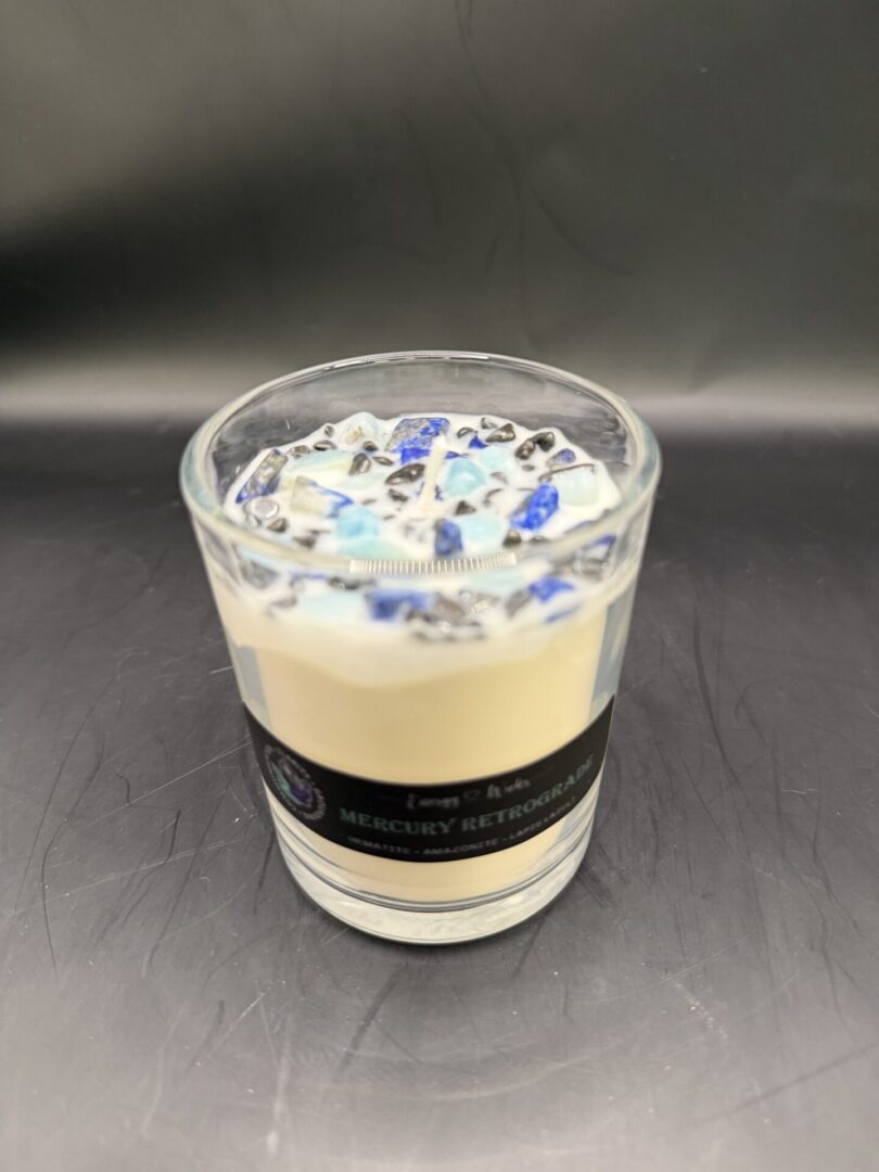 A decorative candle in a glass jar with blue and black stones on top.