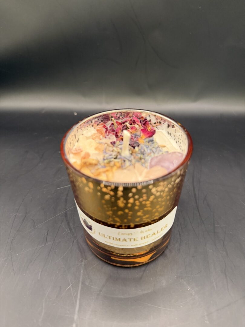 Decorative candle in amber glass with dried flowers and herbs on top.